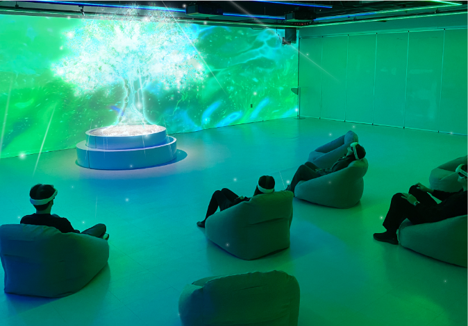 Visitors wearing HMDs engage in the XR meditation experience "Dimension" within a fully immersive exhibition space. The projected visuals feature the Tree of Life, a central symbol in the journey, surrounded by dynamic color therapy visuals. The ambient environment fosters deep relaxation, guiding participants into emotional balance and inner calm.