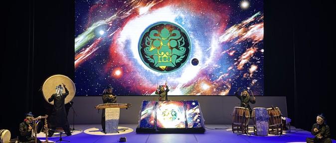 XR performance stage where traditional percussionists perform live before an LED screen displaying the Dochebi emblem